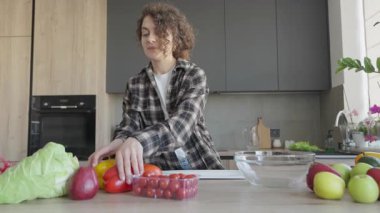 Modern Ev Mutfağı 'nda yemek pişirirken gülümseyen kadın elinde biber tutuyordu. Sağlıklı Malzemeleri Hazırlayan Neşeli Kadın, Parlak Stili İçi Taze Sebzelerle çevrili. Yüksek kalite 4k görüntü