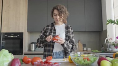 Bright Stylish Kitchen 'da salata hazırlamak için domates soyan genç kadın. Taze içerikli sağlıklı gıda kavramı, modern iç mekan, gevşetilmiş ev yemeği atmosferi. Yüksek kalite 4k görüntü