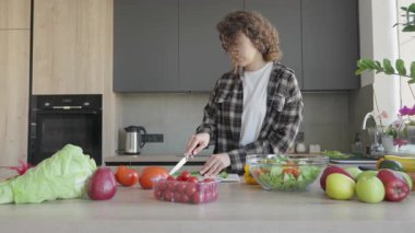 Parlak ev mutfağında sağlıklı yemek için taze salatalık dilimleri hazırlıyorum. Modern mutfağın tahta tahtasında salatalık doğrayan genç kadın.