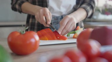 Mutfaktaki tahta kesme tahtasında kırmızı biber dilimleyen kadın. Taze Malzemeler, Sağlıklı Yeme, Ev Yemeği Konsepti, Doğal Işık, Kapalı Kapılar, Organik Sebzeler, Yaşam Tarzı, Mutfak Hazırlığı
