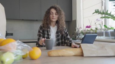 Rahatlamış kadın sabah kahvesini yudumluyor ve evde dizüstü bilgisayar okuyor. Huzurlu Sabah Rutini, Doğal Işık, İçişleri Bakanlığı, Serbest Yaşam Tarzı, Sıcak Atmosfer, Sıcak İçecek. Yüksek kalite 4k görüntü