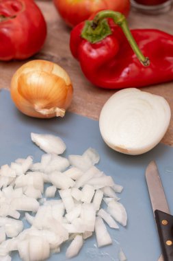 Chopped white onion lies on a blue cutting board, surrounded by fresh whole onions, red bell pepper, and tomatoes. These vibrant ingredients are ready for a healthy homemade meal.