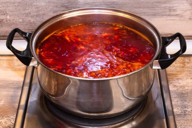 Canlı kırmızı borş elektrikli bir sobanın üzerinde paslanmaz çelik bir tencerede kaynıyor. Sıcak Ukrayna çorbasından buhar yükseliyor, ev yapımı bir yemek..