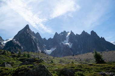 Düşük çalıların ve dağınık kayaların üzerinden yükselen dramatik, kule şekilli dağ silsilesi