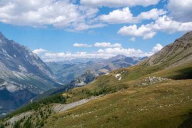 Açık çayırları, kayalık tepeleri ve dramatik bulutları olan huzurlu dağ manzarası.