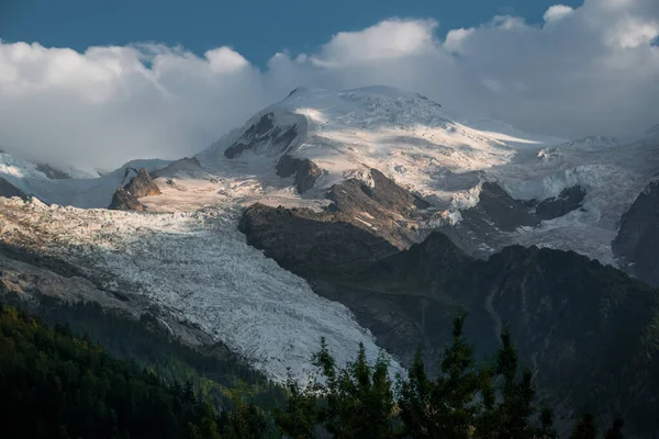 Önünde yeşil yemyeşil bir orman olan karla kaplı Mont Black dağ zirvesi