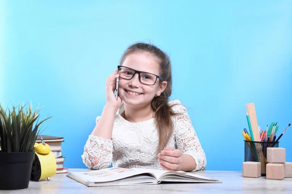 Back to school .Happy cute industrious child is sitting at a desk indoors and talking on the phone. Kid is learning in class.quarantine.Kid is learning in home.