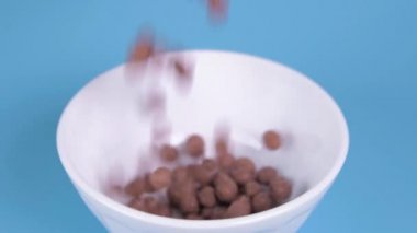 Çikolatalı gevrek. Kahvaltı için çikolata gevrekleri mavi arka plandaki bir kaseye döküldü. Sağlıklı kahvaltı. Bir tabağa taneler dökülüyor.