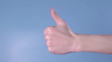 Adam elini çerçeveye sokuyor ve baş parmağın havada olduğunu gösteriyor. Bir adamın elinde mavi arka planda benzer bir işaret var.