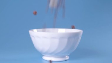 Çikolatalı gevrek. Kahvaltı için çikolata gevrekleri mavi arka plandaki bir kaseye döküldü. Sağlıklı kahvaltı. Bir tabağa taneler dökülüyor.