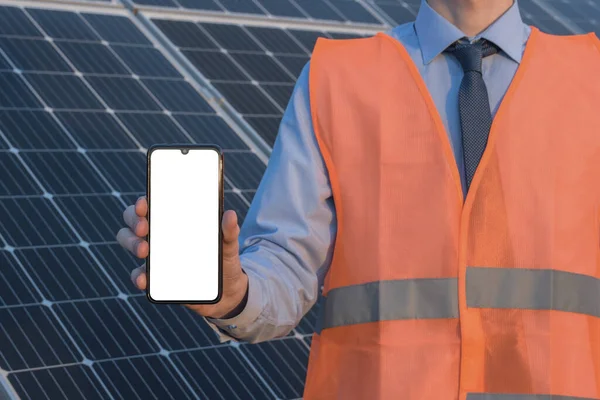 Engineer, man holding mobile phone, smartphone on a background of solar panels. White screen, place for image, text, application.