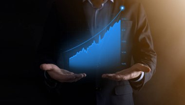 Holografik grafikler ve borsa istatistikleri tutan işadamı kâr elde ediyor. Büyüme planlama ve iş stratejisi kavramı. İyi ekonomi formunun dijital ekran görüntüsü.
