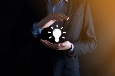 Koruyucu jestleri olan iş adamı elinde ampul ikonu ile yenilikçi teknoloji ve yaratıcılık içeren yeni fikirler üretiyor.