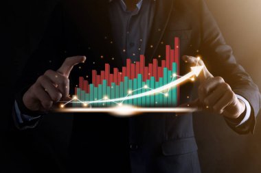 İş adamı, karanlık arka planda okları olan, istatistik, grafik ve grafiklerin büyüyen sanal bir hologramını tutuyor ve gösteriyor. Borsa. İş büyümesi, planlama ve strateji kavramı