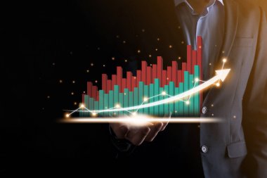 İş adamı, karanlık arka planda okları olan, istatistik, grafik ve grafiklerin büyüyen sanal bir hologramını tutuyor ve gösteriyor. Borsa. İş büyümesi, planlama ve strateji kavramı