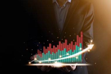 İş adamı, karanlık arka planda okları olan, istatistik, grafik ve grafiklerin büyüyen sanal bir hologramını tutuyor ve gösteriyor. Borsa. İş büyümesi, planlama ve strateji kavramı
