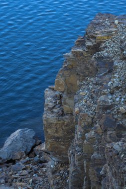 Su kenarındaki kayalar, gölün, nehrin, denizin ve okyanusun arka planında. Mavi berrak su. Yapay su rezervleri.