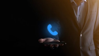 Siyah arka planda takım elbiseli bir işadamı akıllı telefon ikonuna sahip. Şimdi İş İletişim Destek Merkezi Müşteri Hizmetleri Teknolojisi Konseptini Ara.