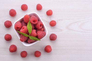 Ahşap zemin üzerinde yeşil yapraklar olan bir kase taze ahududu. Üst görünüm.