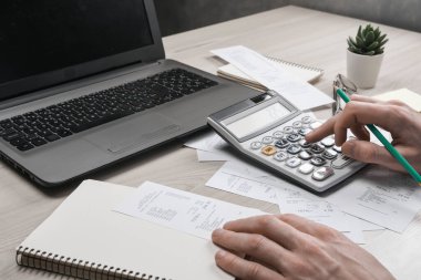 Hesap makinesi ve yazı makinesi kullanan bir adam ev ofisinin maliyet ve vergilerini hesaplayarak not alır. İşadamı iş yerinde evrak işleriyle uğraşıyor.