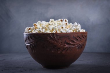 Gri arka plandaki masada bir kasede tuzlanmış patlamış mısır. Ön görünüm.