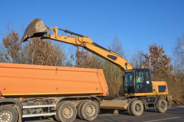 Bir kova kazıcı yol kenarını temizliyor. Yol çalışıyor. Yeni bir yol açıyorum. Kazı kil ve bir taş yükleniyor