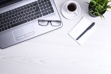 Ofis çalışma alanının en üst görüntüsü, dizüstü bilgisayarı, klavyesi, gözlükleri, telefonu ve bir fincan kahvesi olan tahta masa masası..
