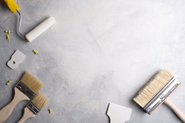 Gri beton arka planda boya yapmak için macun, fırça ve silindirler kullanılıyor. Üst görünüm