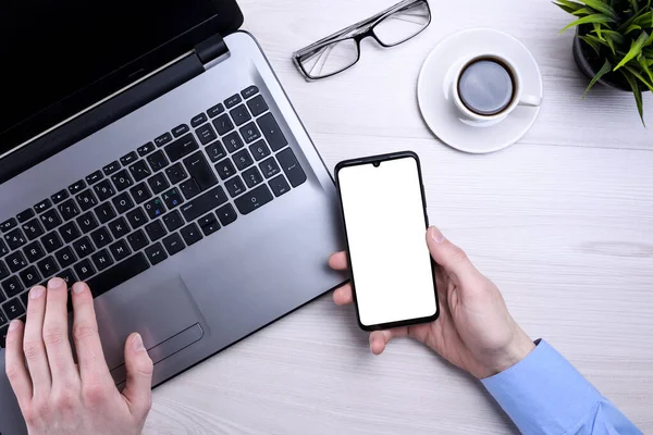 Businessman, man works at desktop on laptop and uses mobile phone. Top view, smartphone, glasses, cup of coffee. Mock up.