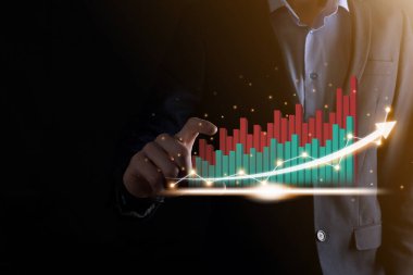 İş adamı, karanlık arka planda okları olan, istatistik, grafik ve grafiklerin büyüyen sanal bir hologramını tutuyor ve gösteriyor. Borsa. İş büyümesi, planlama ve strateji kavramı