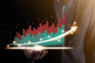 İş adamı, karanlık arka planda okları olan, istatistik, grafik ve grafiklerin büyüyen sanal bir hologramını tutuyor ve gösteriyor. Borsa. İş büyümesi, planlama ve strateji kavramı