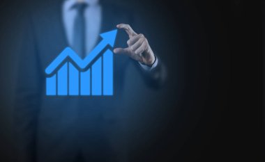 İş adamı elinde tablet tutuyor ve karanlık zemin üzerinde ok bulunan istatistik, grafik ve grafiklerin büyüyen sanal hologramını gösteriyor. Borsa. İş büyümesi, planlama ve strateji kavramı