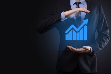 İş adamı elinde tablet tutuyor ve karanlık zemin üzerinde ok bulunan istatistik, grafik ve grafiklerin büyüyen sanal hologramını gösteriyor. Borsa. İş büyümesi, planlama ve strateji kavramı