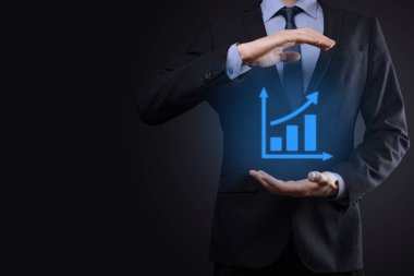 İş adamı elinde tablet tutuyor ve karanlık zemin üzerinde ok bulunan istatistik, grafik ve grafiklerin büyüyen sanal hologramını gösteriyor. Borsa. İş büyümesi, planlama ve strateji kavramı