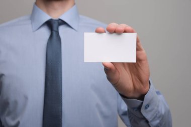İş adamı, iş adamının el ele tutuşması. Gri arka planda yakın plan görüntüsü var. Boş bir kağıt parçası göster. Kağıt ziyareti kartı.