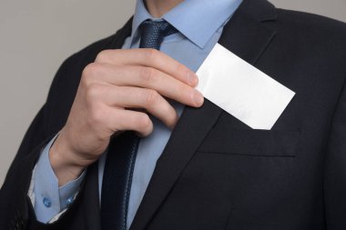 İş adamı, iş adamının el ele tutuşması. Gri arka planda yakın plan görüntüsü var. Boş bir kağıt parçası göster. Kağıt ziyareti kartı.