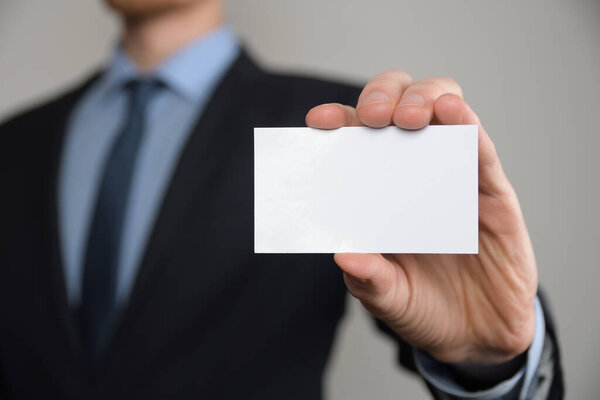 Businessman ,Business Man's hand hold showing business card - close up shot on grey background. Show a blank piece of paper. Paper visit card.