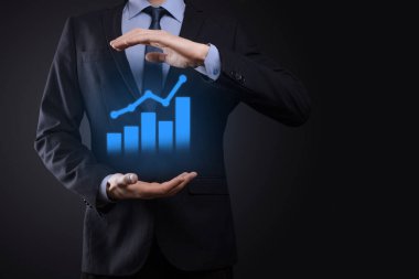 İş adamı elinde tablet tutuyor ve karanlık zemin üzerinde ok bulunan istatistik, grafik ve grafiklerin büyüyen sanal hologramını gösteriyor. Borsa. İş büyümesi, planlama ve strateji kavramı