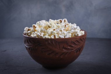 Gri arka plandaki masada bir kasede tuzlanmış patlamış mısır. Ön görünüm.