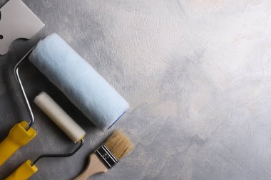 Gri beton arka planda boya yapmak için macun, fırça ve silindirler kullanılıyor. Üst görünüm
