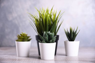 Yapay çiçekler, ahşap arka plandaki bir tencerede farklı şekillerde çimenler. Kopya alanı ve metin ile kapatın..