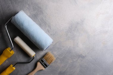 Gri beton arka planda boya yapmak için macun, fırça ve silindirler kullanılıyor. Üst görünüm