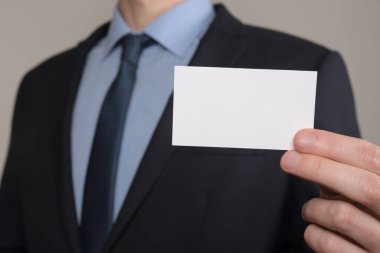 İş adamı, iş adamının el ele tutuşması. Gri arka planda yakın plan görüntüsü var. Boş bir kağıt parçası göster. Kağıt ziyareti kartı.