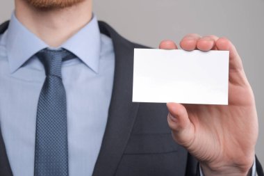 İş adamı, iş adamının el ele tutuşması. Gri arka planda yakın plan görüntüsü var. Boş bir kağıt parçası göster. Kağıt ziyareti kartı.