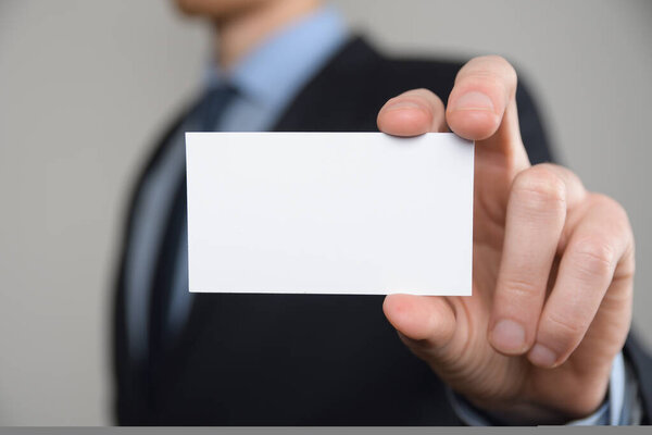 Бизнесмен, рука бизнесмена показывает визитную карточку - крупный план на сером фоне. Покажите чистый лист бумаги. Карточка посещения.