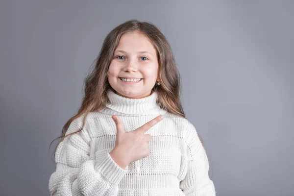 스웨터를 누르스름 머리를 매력적 소녀의 모습이 미소를 스튜디오 배경에 가리킨다 — 스톡 사진