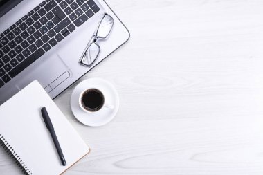 Ofis çalışma alanının en üst görüntüsü, dizüstü bilgisayarı, klavyesi, gözlükleri, telefonu ve bir fincan kahvesi olan tahta masa masası..