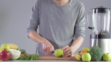 Mutfaktaki mutfak masasındaki genç bir adam meyve suyu için elma kesiyor. Karıştırıcıda smoothie pişiriyorum.