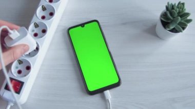 Şarj edilen cep telefonu, akıllı telefon. Adam ahşap zemine uzatma kablosu soketine cep telefonu şarjı koymuş. Yükleyici USB C şarj cihazı devrede. Yeşil ekran..