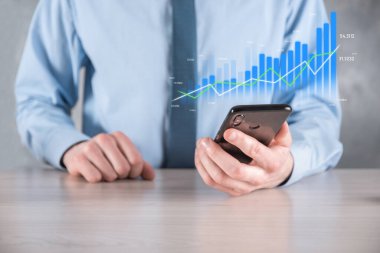 İş adamı elinde pozitif kar artışı olan bir grafik tutuyor. Grafik büyümesi ve grafik artışı işlerinde olumlu göstergeler. Daha kârlı ve büyüyen.